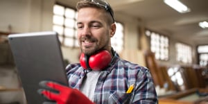 Portrait of middle aged professional worker carpenter with ear protectors using tablet in carpentry workshop