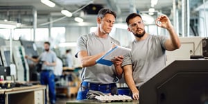 Two cnc machine operators examining finished products and writing notes in industrial facility